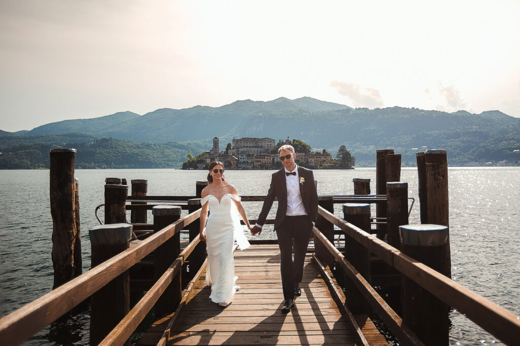 Bride and groom walking on a jetty with San Giulio island as background