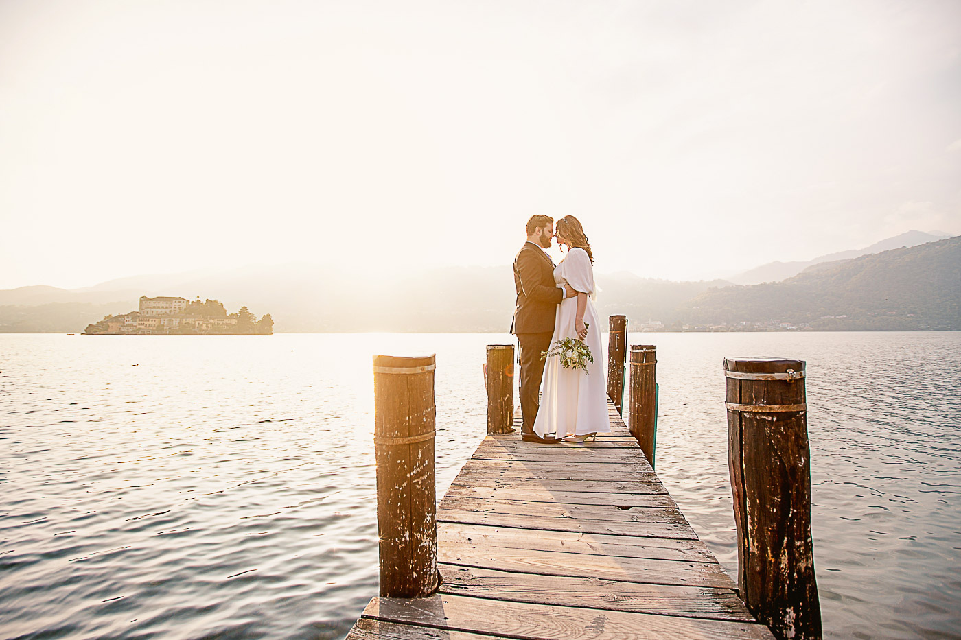 Romantic hug from groom to the bride on a jetty by the lake Orta during the sunset