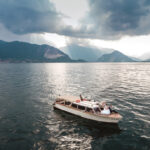 Lake Maggiore wedding photographer, drone shot with bride and groom on boat in the middle of Lake Maggiore and a stunning view of the lake and Alps